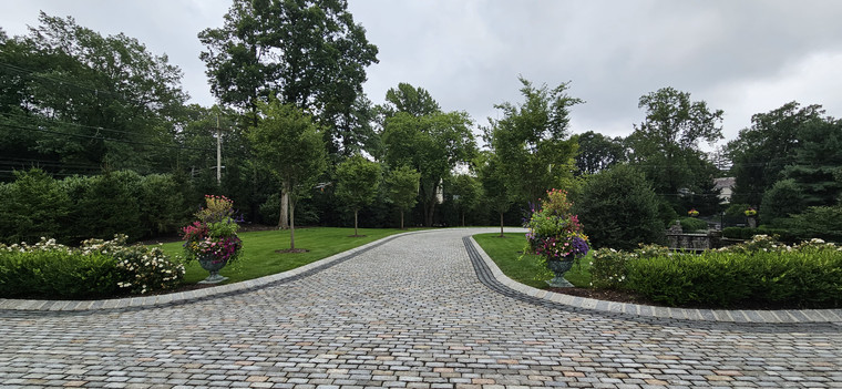 Cobblestone driveway lined with stone curbing, urn planters, and mature trees
