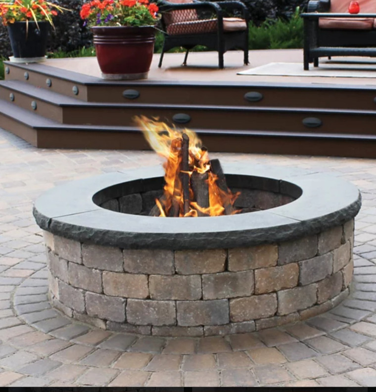 Paver patio fire pit with burning logs and deck steps beyond