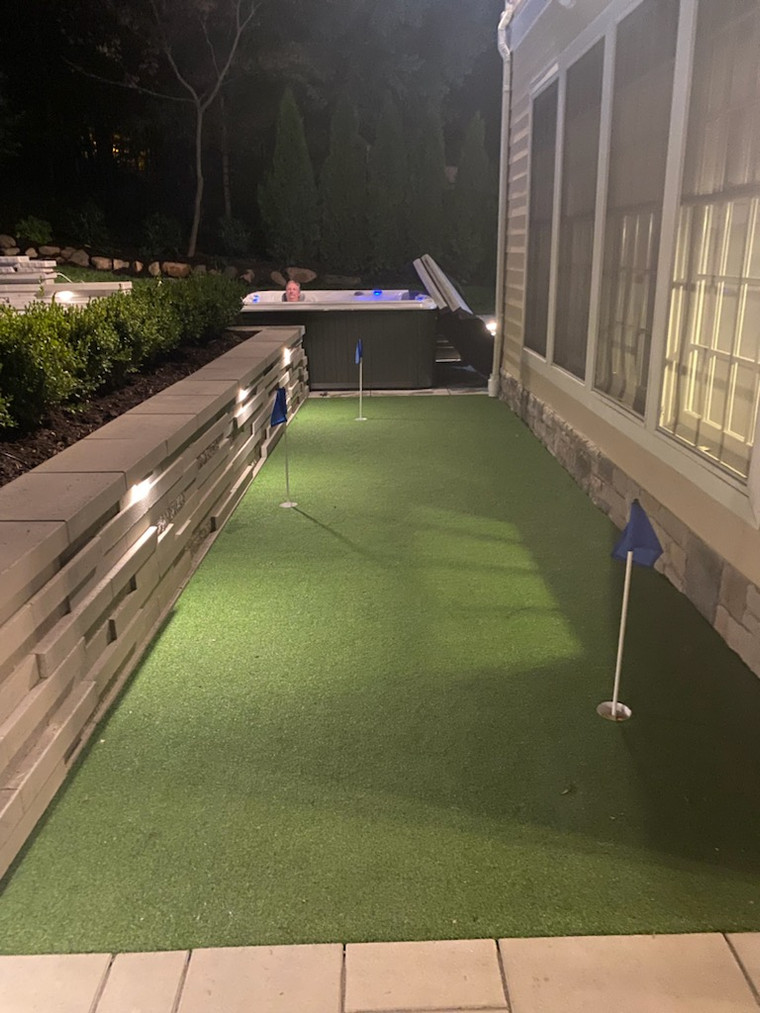 Nighttime backyard putting green beside a hot tub with lighted retaining wall