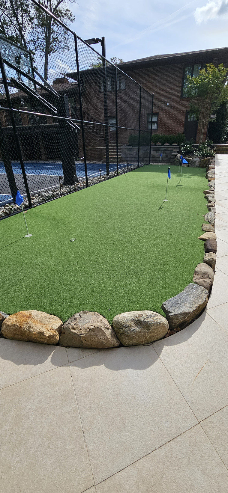 Multi-hole putting green with boulder edging beside a tennis court