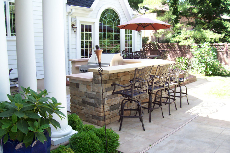Stone outdoor bar and grill station with swivel stools and umbrella