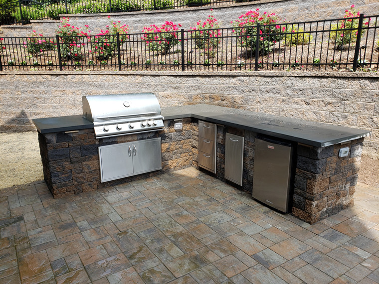 L-shaped outdoor kitchen with grill and refrigerator beside a rose garden