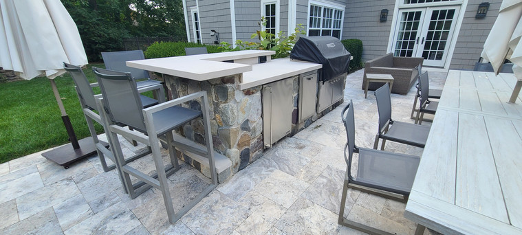 Modern stone outdoor kitchen with curved bar and patio dining set