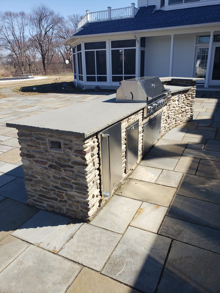 Long stone outdoor kitchen with concrete countertop and built-in grill