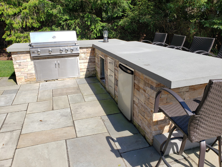 Stacked-stone outdoor kitchen with grill, fridge, and bar overhang
