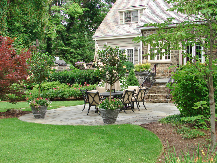 Curved bluestone patio with garden dining surrounded by manicured shrubs