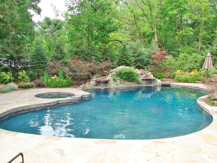 Freeform pool with raised spa, rock waterfall, and woodland garden surround