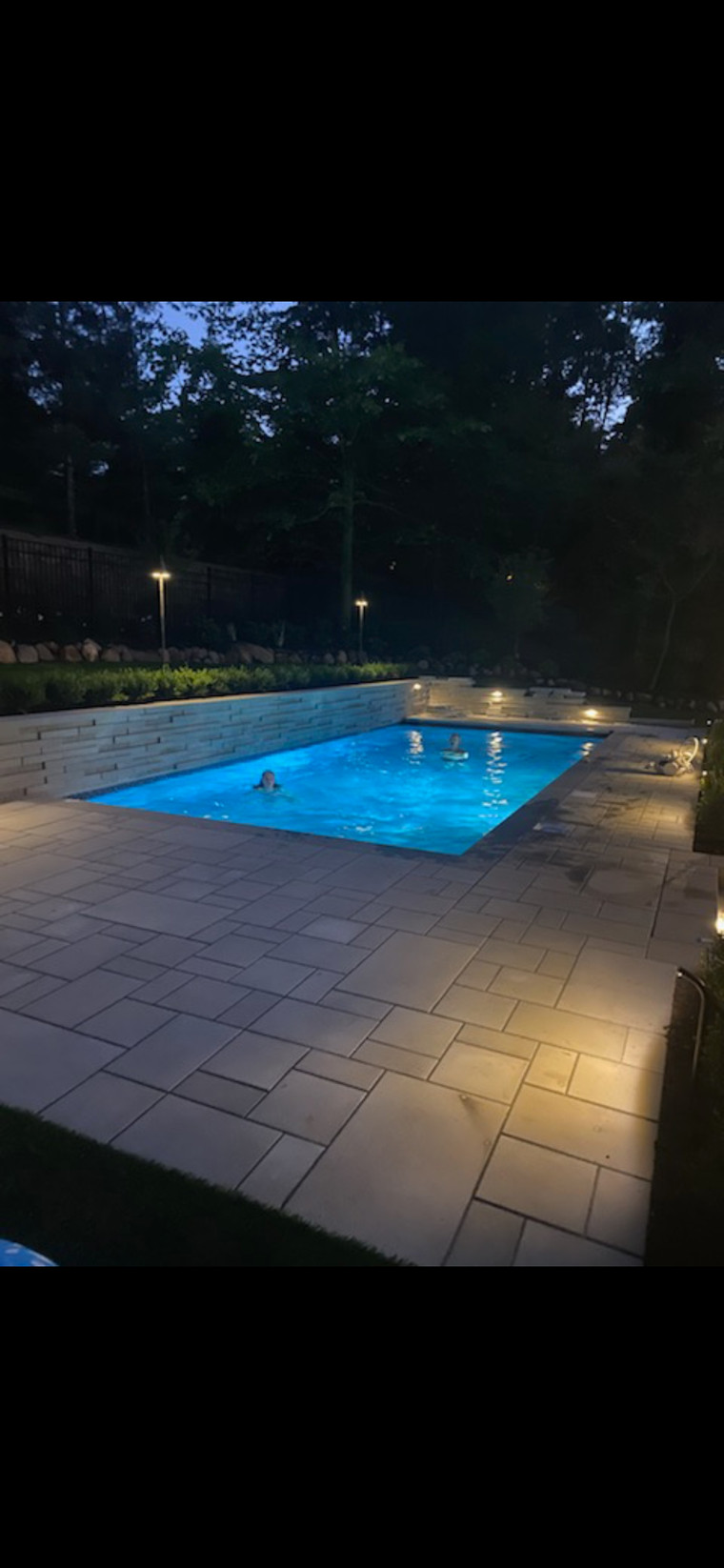 Bluestone pool deck with stacked-stone wall and underwater lighting at dusk