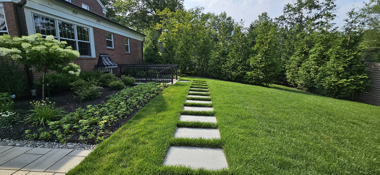 Square bluestone stepping stones across a manicured lawn beside a planted border