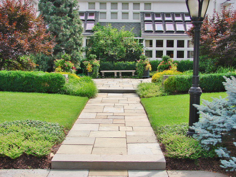Formal bluestone walkway flanked by clipped hedges leading to a garden bench
